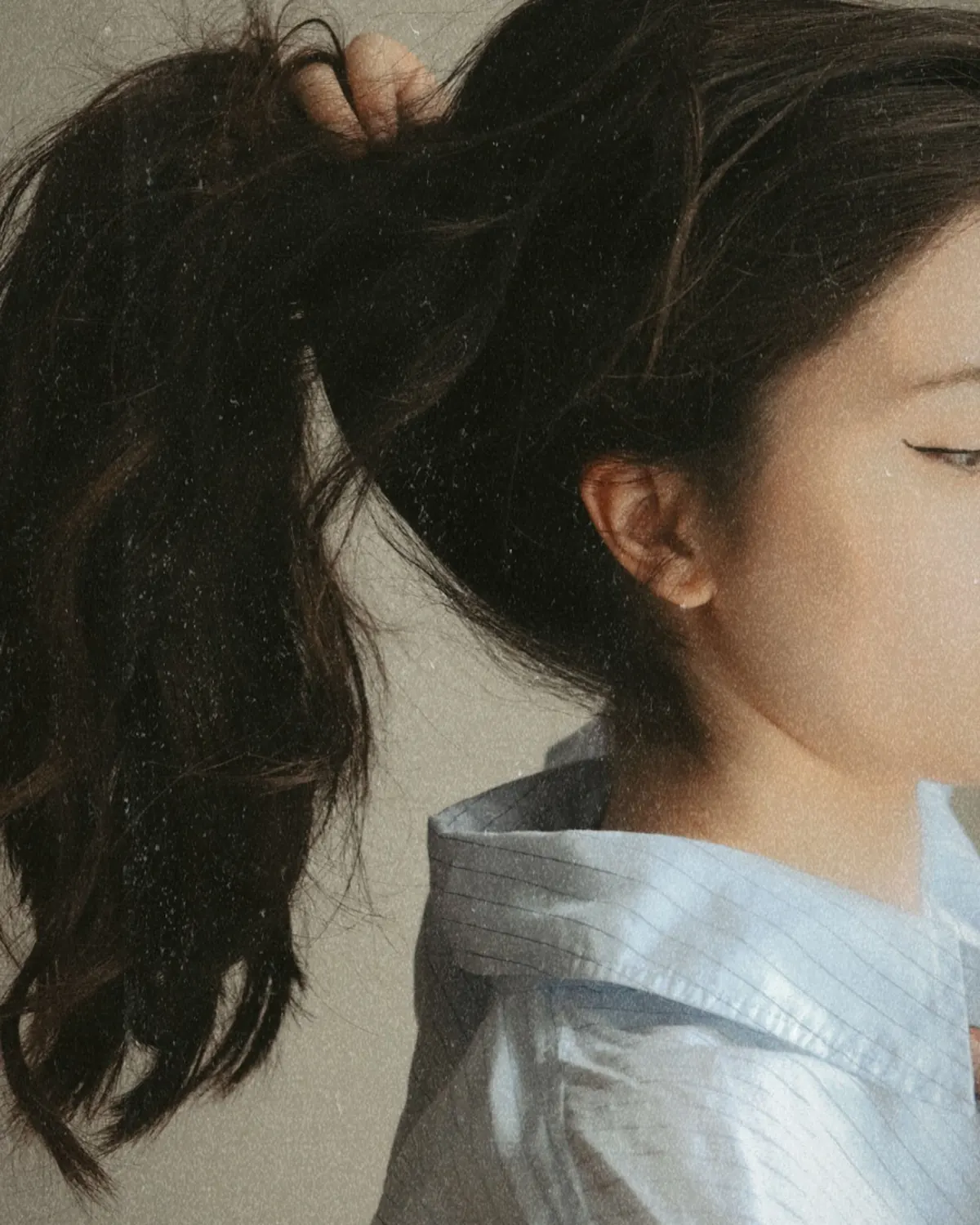 Coleta alta de pelo oscuro sobre una camisa azul clara