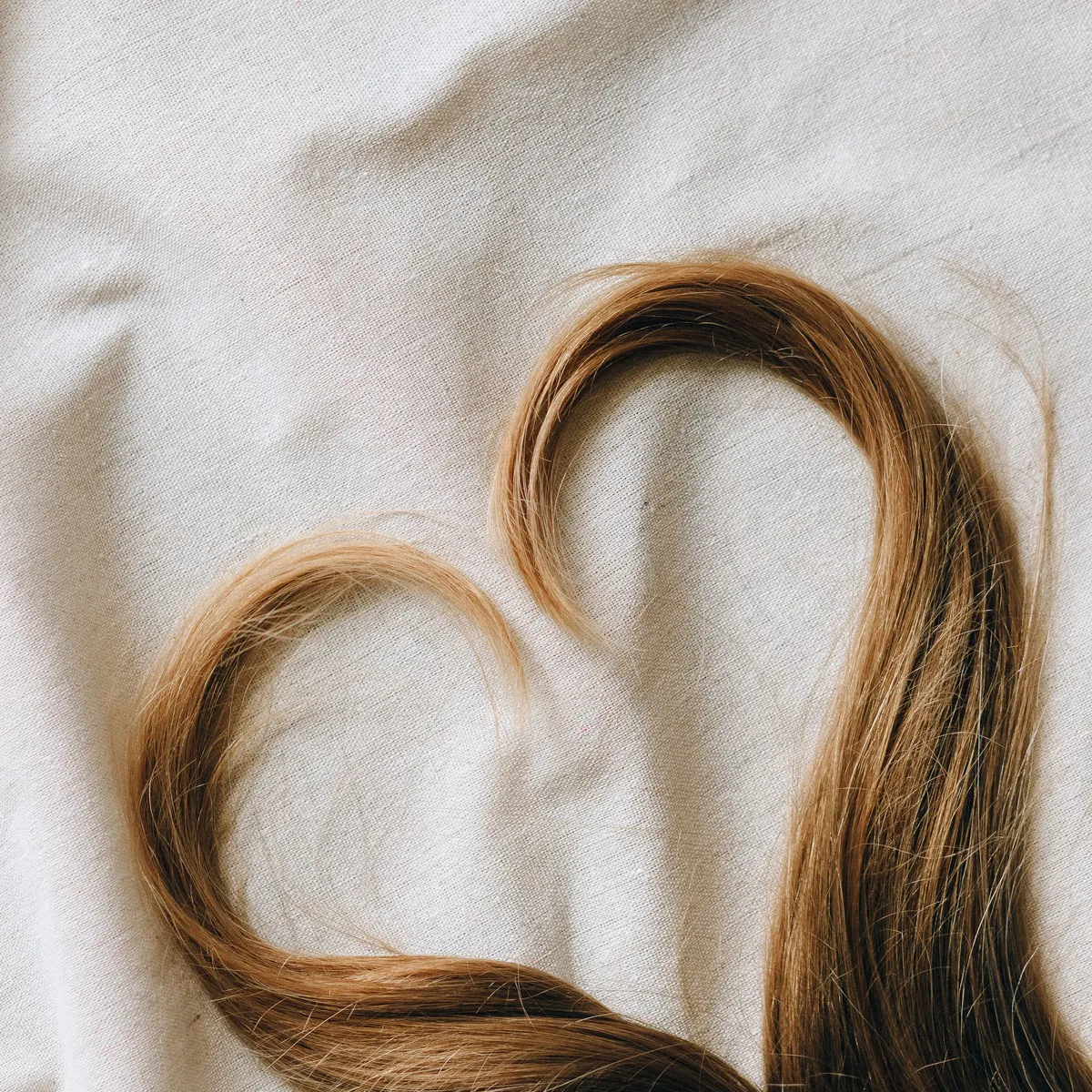 Mechón de pelo rubio formando un corazón sobre una tela clara