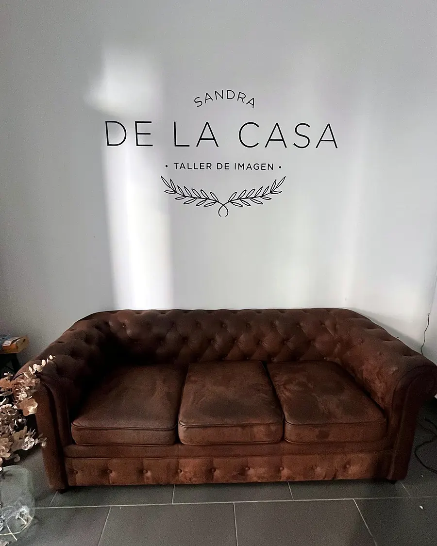Pared blanca con el logo de Sandra de la Casa Taller de Imagen sobre un sofá chester marrón