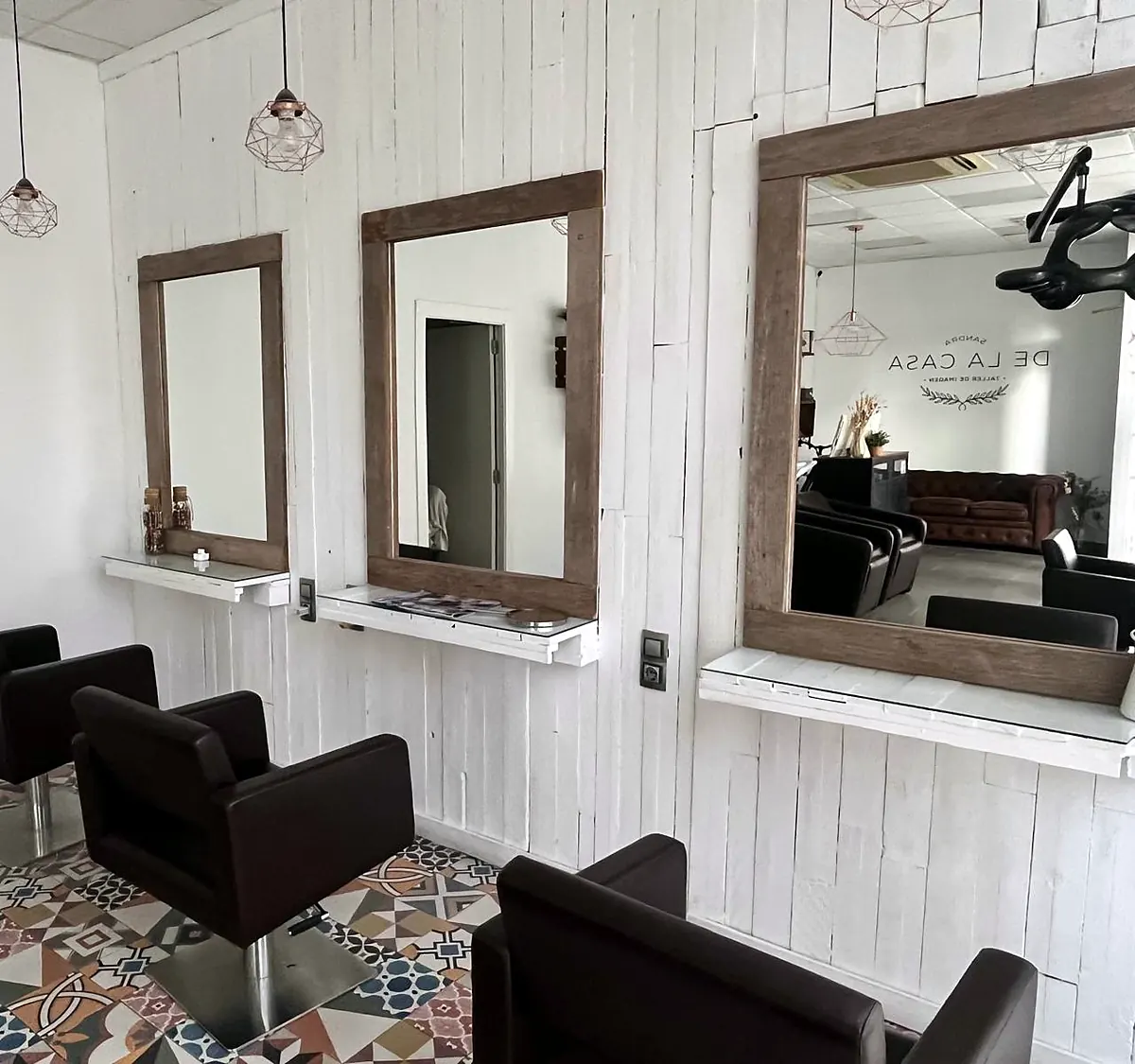 Puestos de corte con espejos de marco de madera y sillones negros sobre suelo de mosaico
