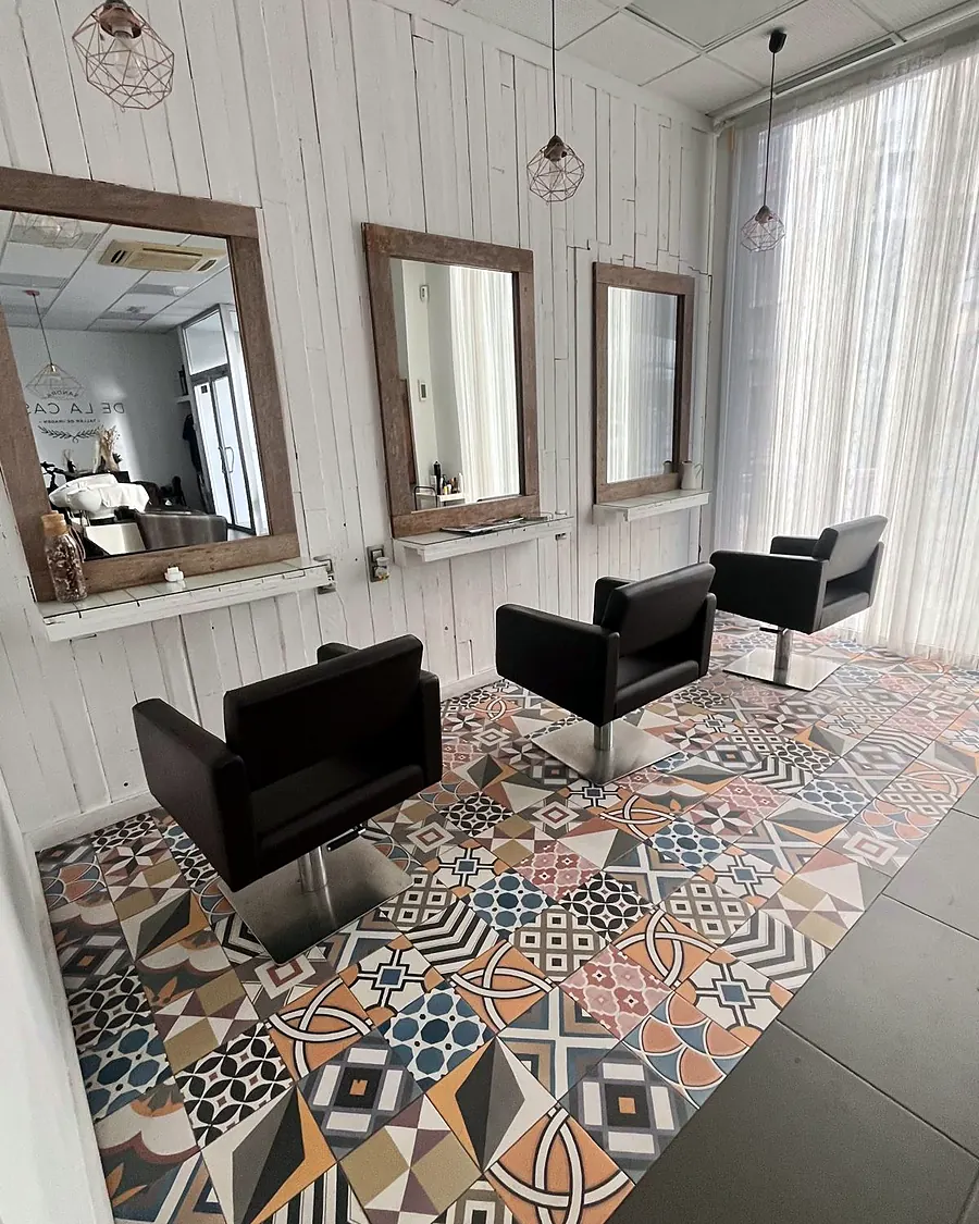 Tres espejos con marco de madera y sillones negros sobre un suelo de mosaico de colores