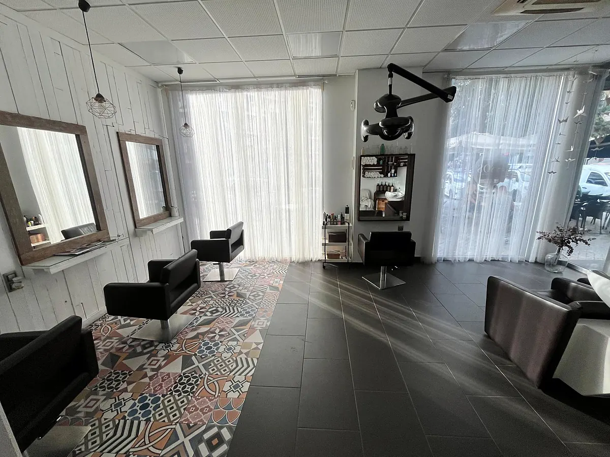 Sala del salón con luz natural entrando por las cortinas, suelo de mosaico de colores y sillones de peluquería negros