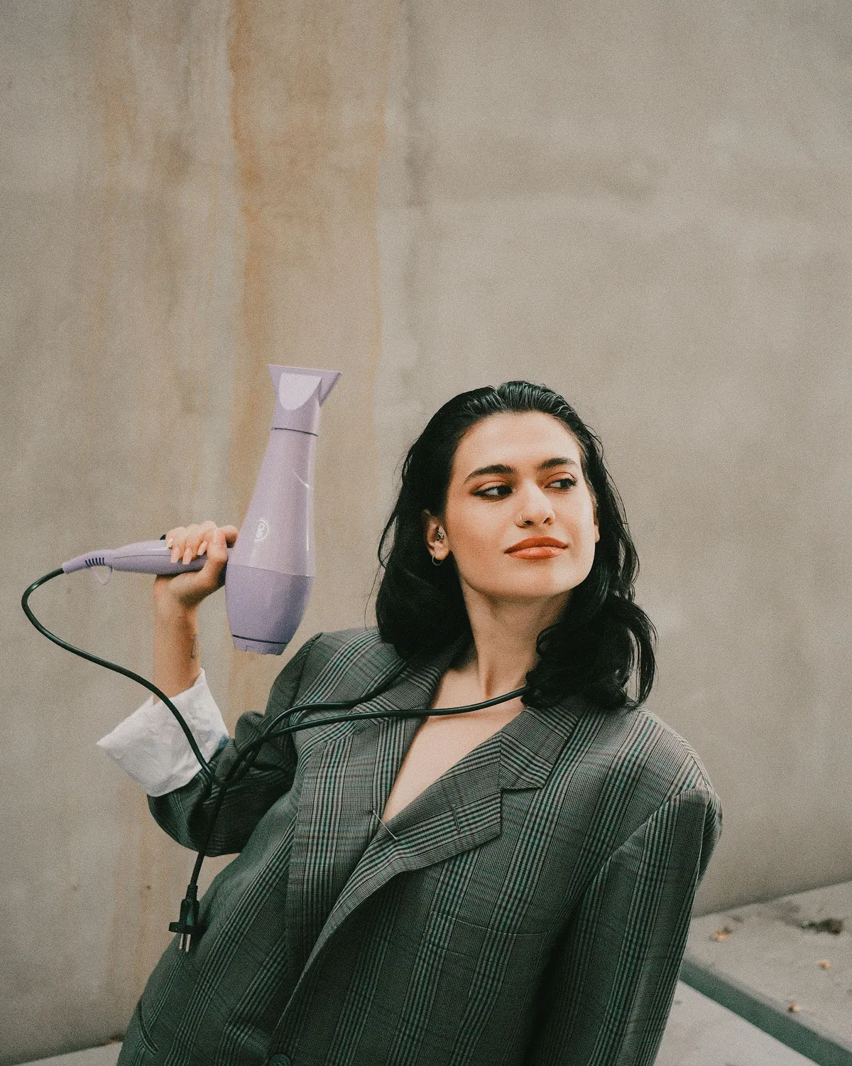 Mujer con blazer verde sosteniendo un secador de pelo en actitud editorial